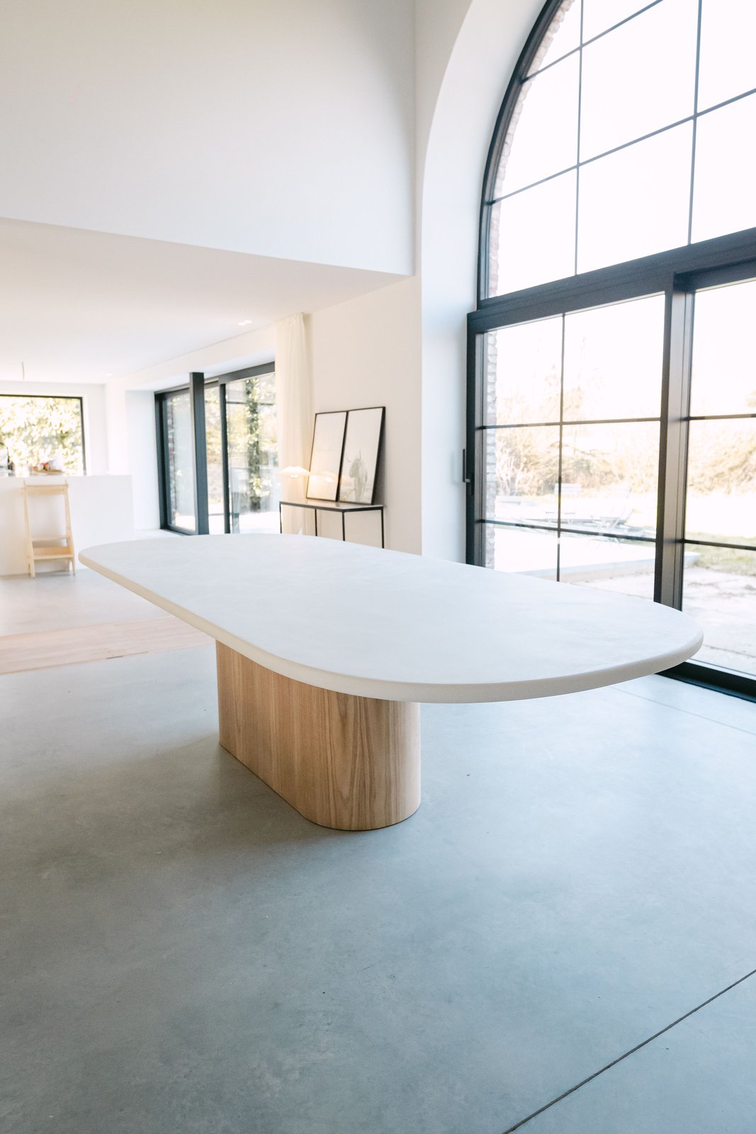 Grande table à manger ovale en Mortex® crème, piètement chêne, sous la verrière d'un loft belge