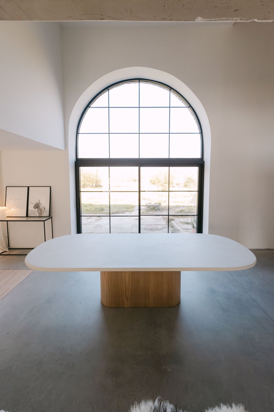 Table ovale en Mortex® crème devant une fenêtre cintrée, piètement chêne cylindrique