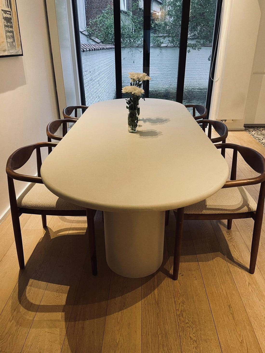Table ovale en Mortex® et chaises en noyer dans une salle à manger lumineuse